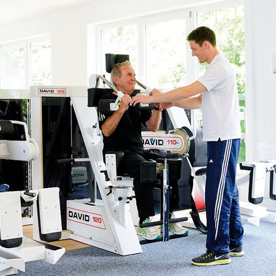 Medizinische Trainingstherapie: Trainer unterstützt Senior bei Übung am DAVID Gerät während MTT-Training im ZAR Aalen.