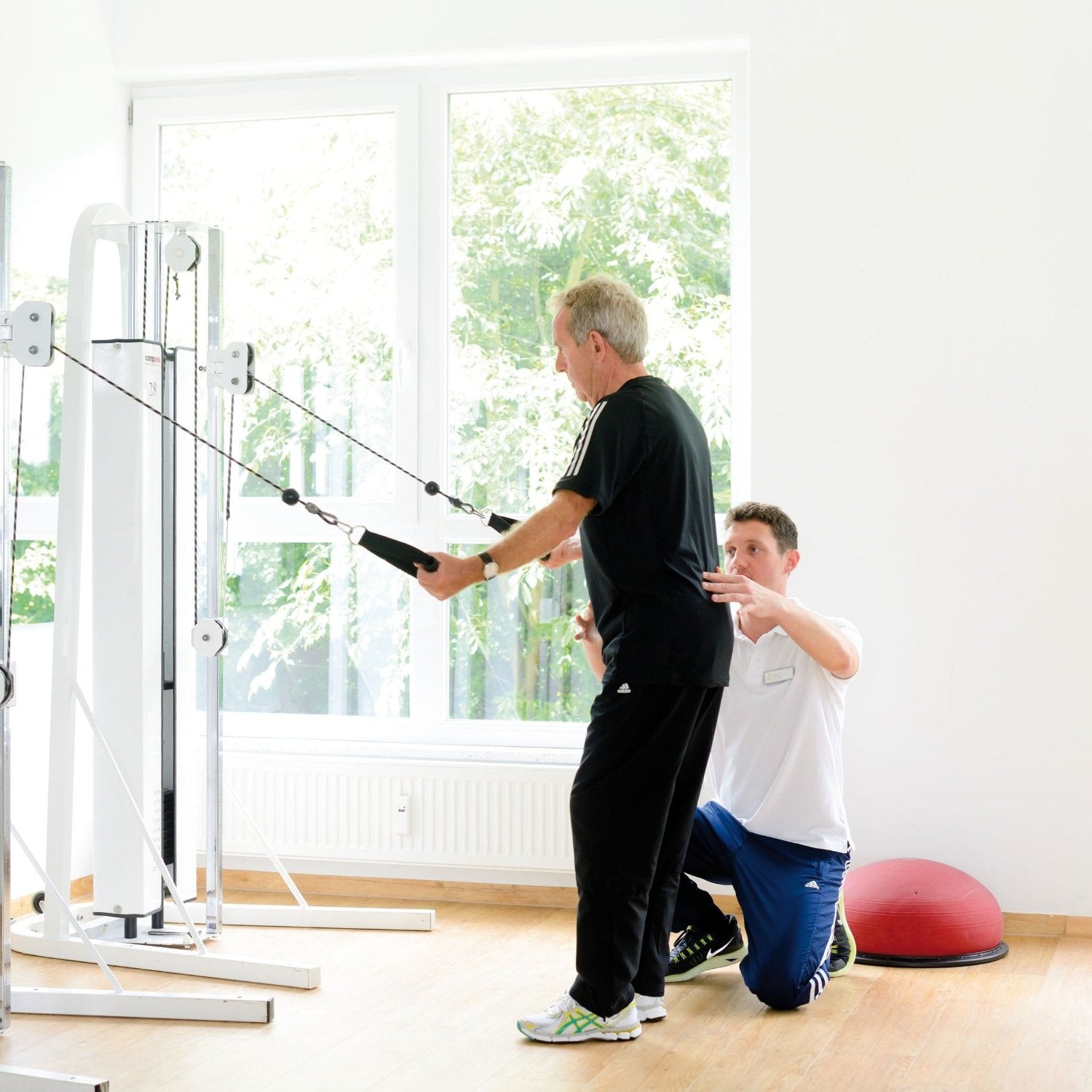 Medizinische Trainingstherapie: Physiotherapeut leitet Patient bei Kabelzugübung an während MTT-Training im ZAR Aalen.